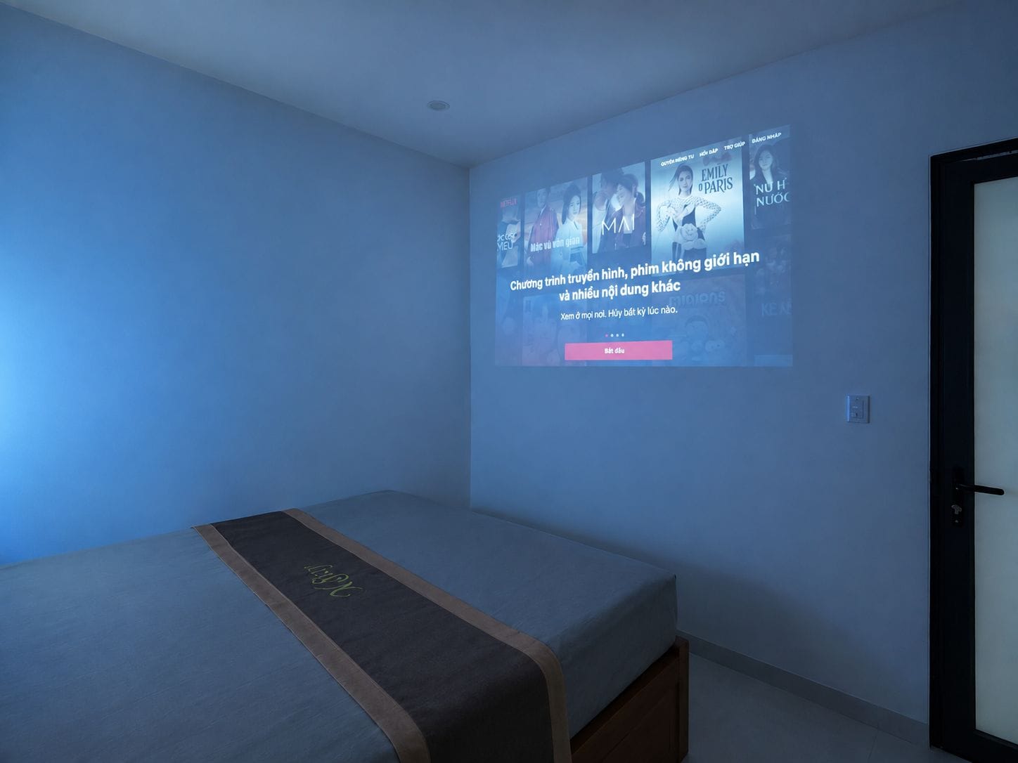 Una camera da letto con un letto, un proiettore a muro che mostra poster di film e una porta.