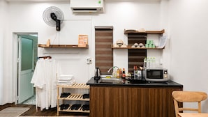 Une chambre d’hôtel comprenant un lit, une chaise en bois, une petite kitchenette avec un four à micro-ondes, un évier et un ventilateur.