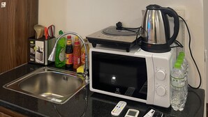 Una cocina con microondas, hervidor de agua y varios utensilios. Hay repisas sobre la encimera con platos y un menú impreso.