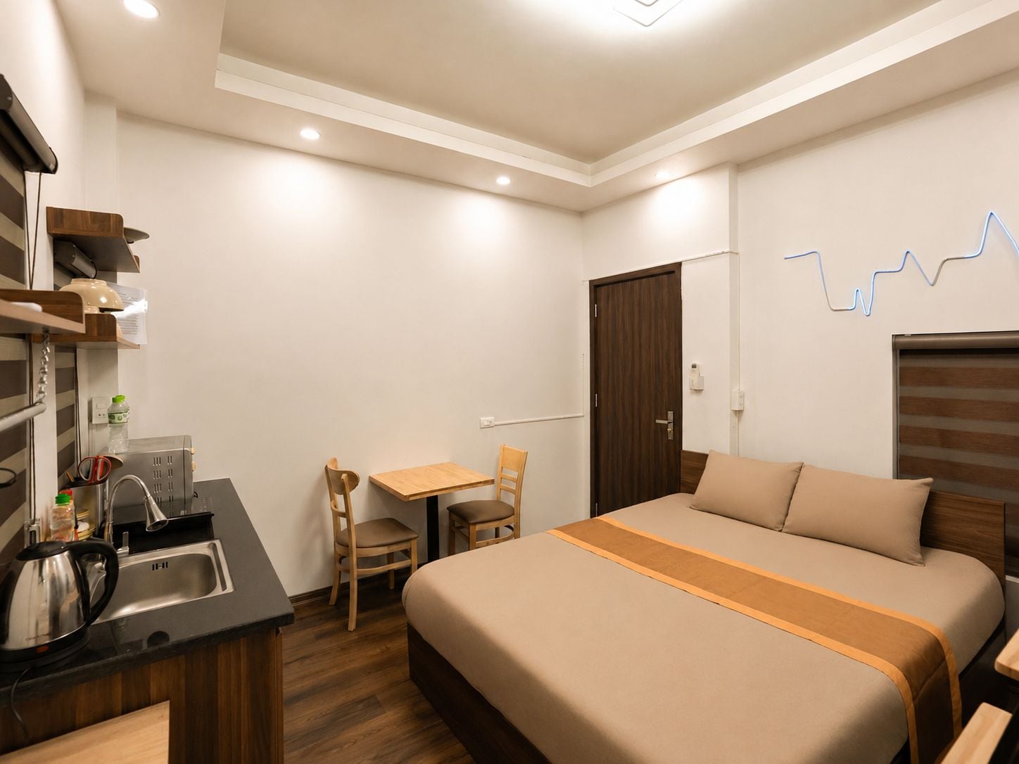 A hotel room with a kitchenette, a bed, a desk, and a chair.