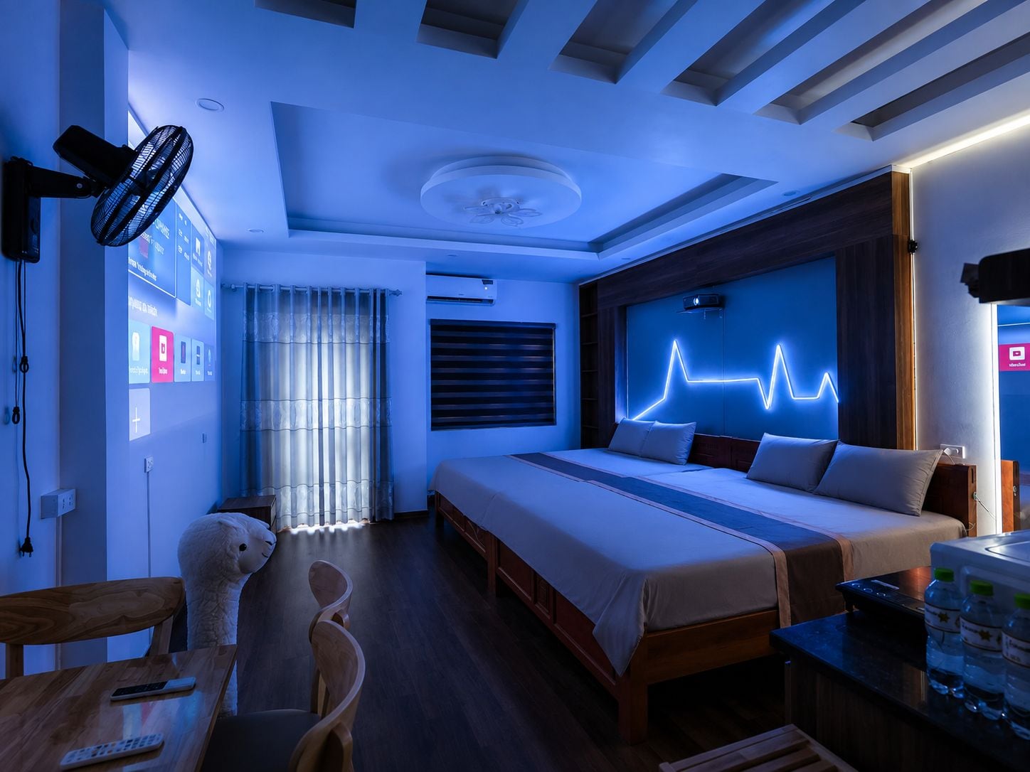 Une chambre d’hôtel moderne équipée d’un lit, d’une table de chevet et d’un projecteur fixé au mur.