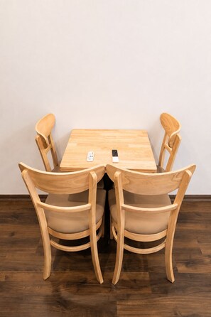 A wooden dining table with four chairs, a remote control, and a smartphone on the table. - X-Stay Thư Trung (Hai Phong)