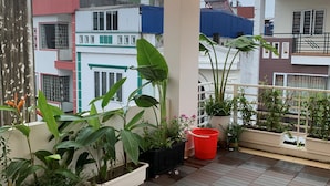 Un balcón con plantas en macetas, luces de cuerda y piso de baldosas.