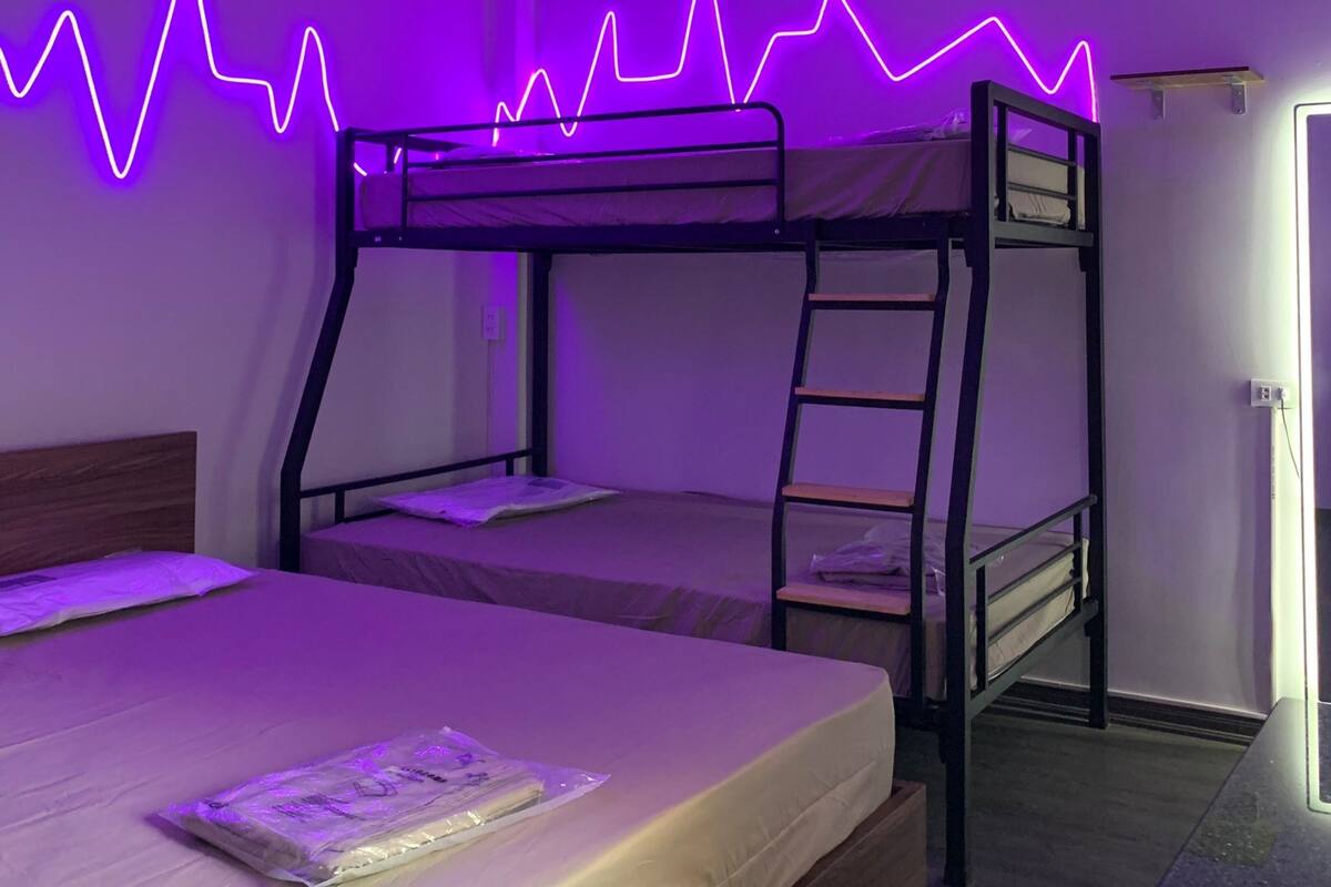 A room with bunk beds, a desk, and a neon light wall.