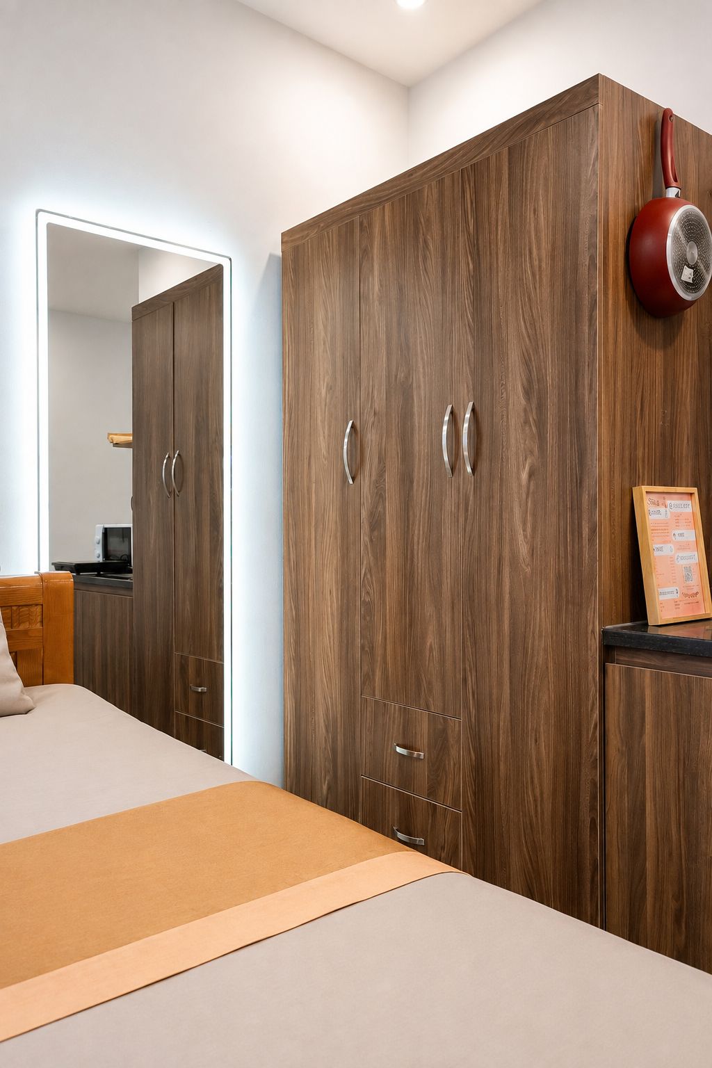 A bedroom with a large wardrobe, a bed, and a red kettle on the wall.