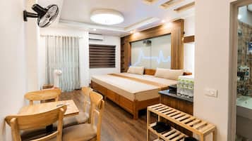 A modern hotel room with a bed, a desk, chairs, a fan, and a shoe rack.