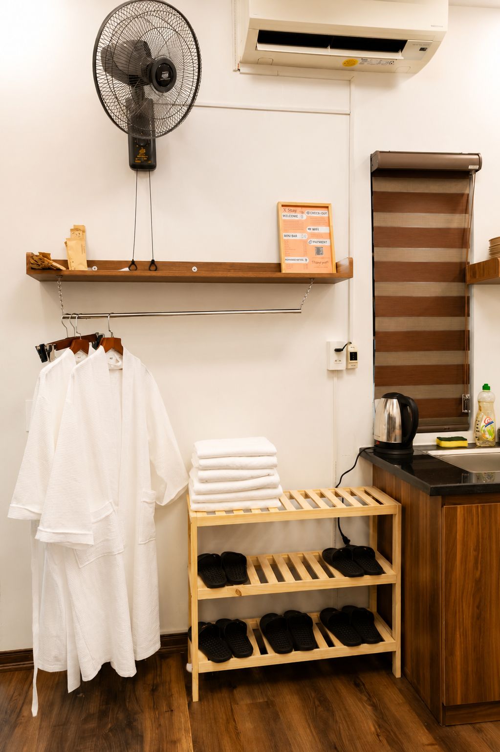 A hotel room with a fan, air conditioning unit, towel rack, shelf with toiletries, and a shoe rack.