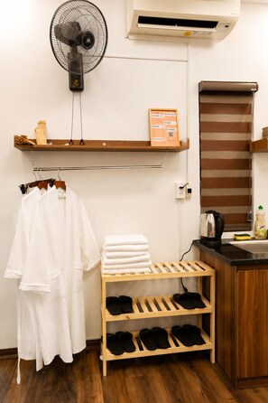 A hotel room with a fan, air conditioning unit, towel rack, shelf with toiletries, and a shoe rack. - X-Stay Thư Trung (Hai Phong)