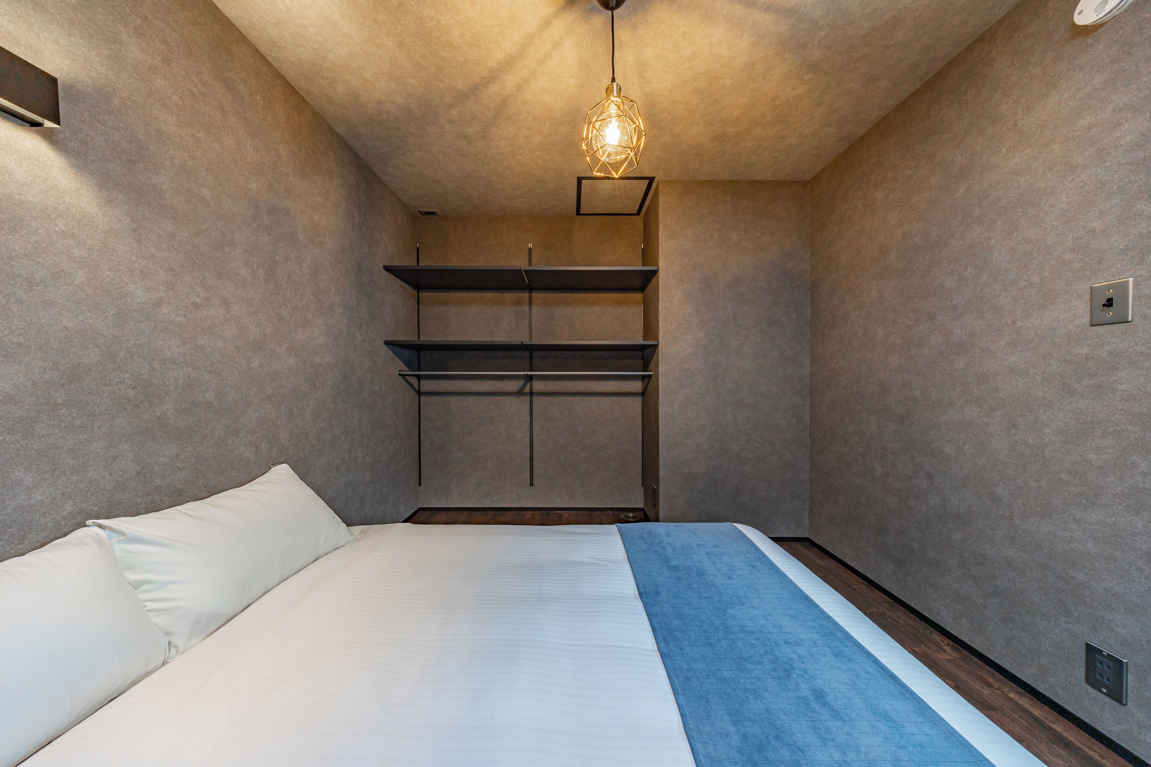 A bedroom with a bed, a wardrobe, and a hanging light fixture.
