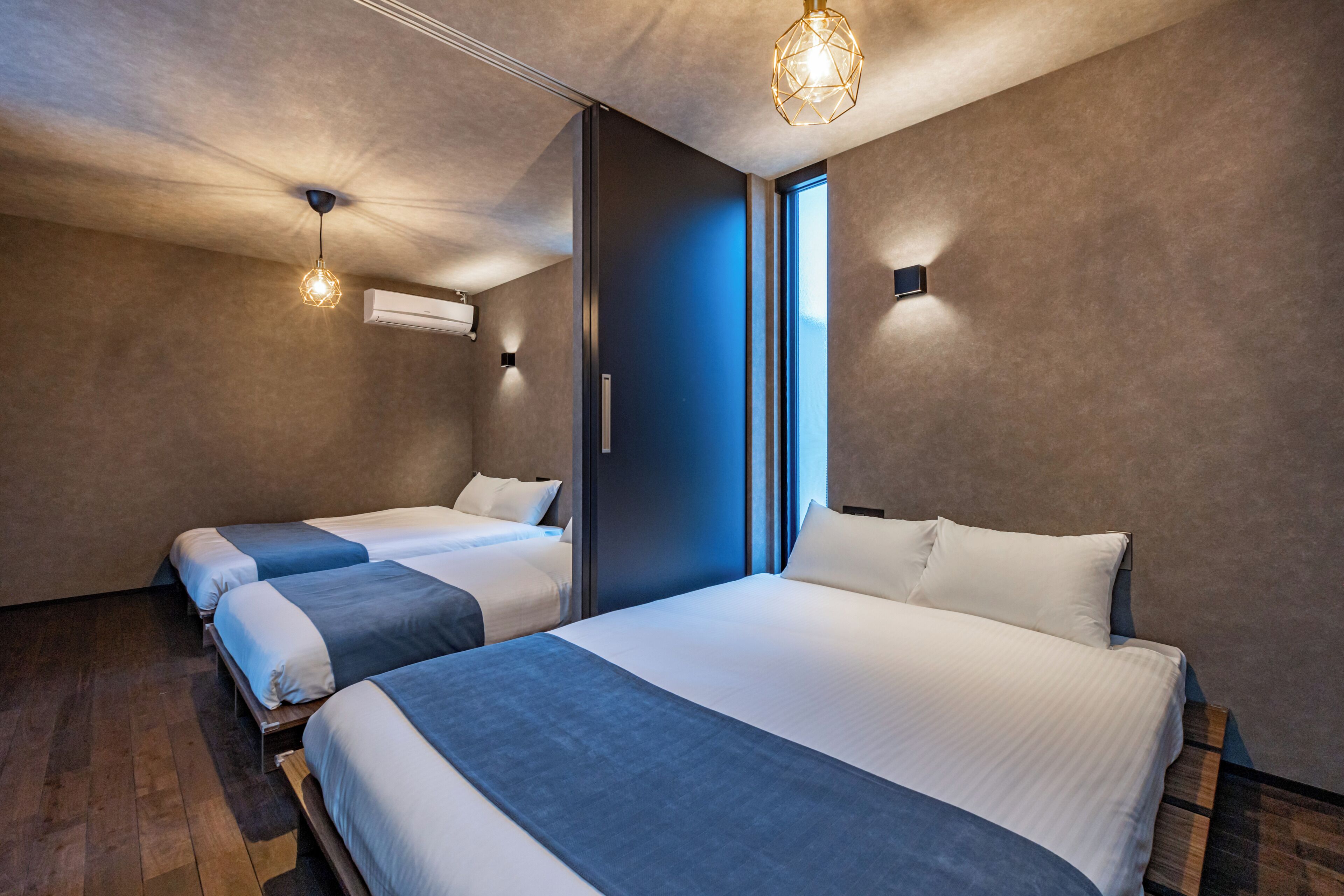 Une chambre d’hôtel moderne avec deux lits, une grande fenêtre et un luminaire au plafond au design géométrique original.