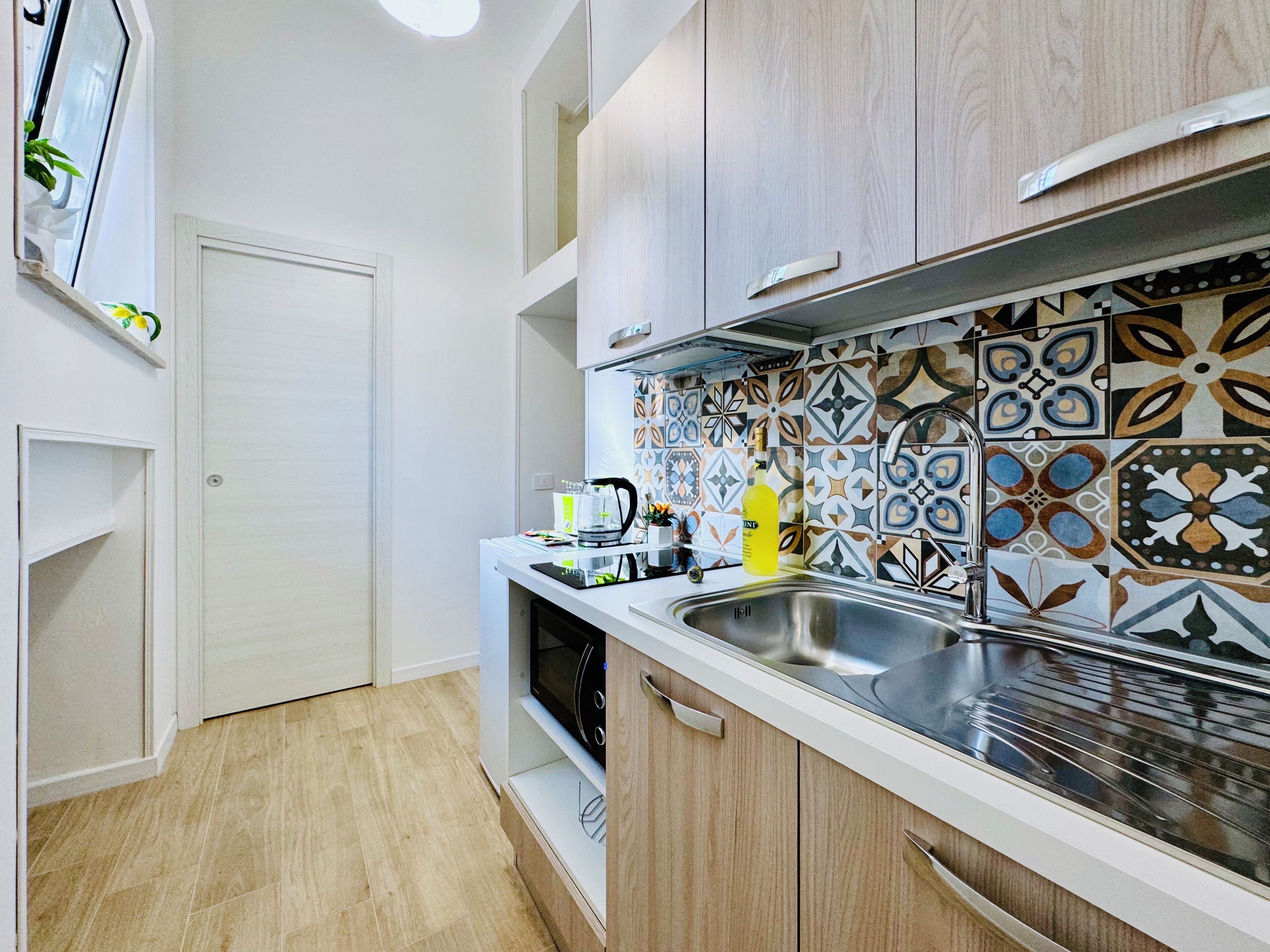 A modern kitchen with a stainless steel sink, wooden cabinets, and patterned backsplash tiles.