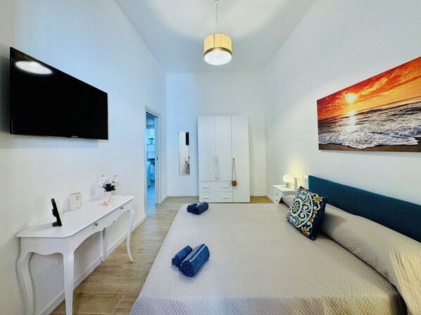 A modern hotel room with a bed, a desk, a TV, and a painting of a sunset. - YourHome - La Casa di Ninì (Sant'Agnello)