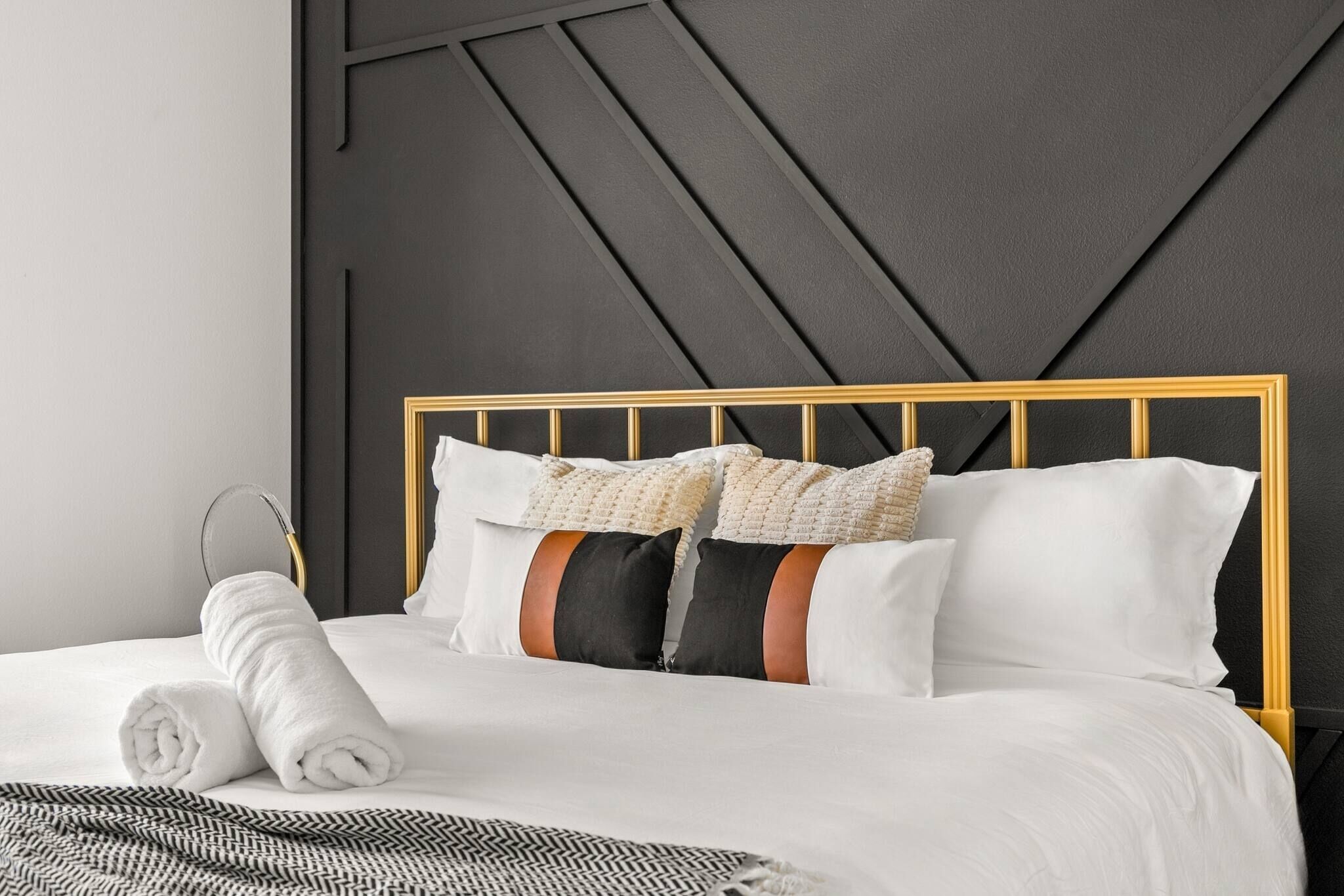 A neatly made bed with a gold headboard, white bedding, and a rolled white towel.