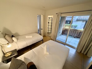 A hotel room with a bed, a bedside table with a lamp, a window with curtains, and a view of the outside. - Heart of Carlsbad 2 bed 2 bath with Pool + Hot Tub (Carlsbad)