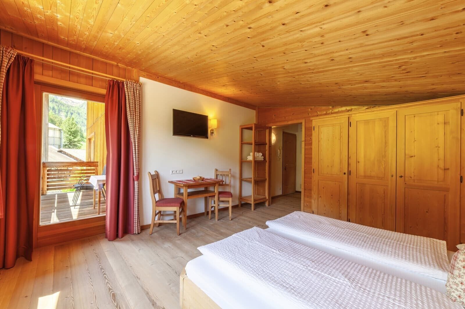 Una baita in legno con un letto, un tavolo con sedie, un televisore e un armadio.