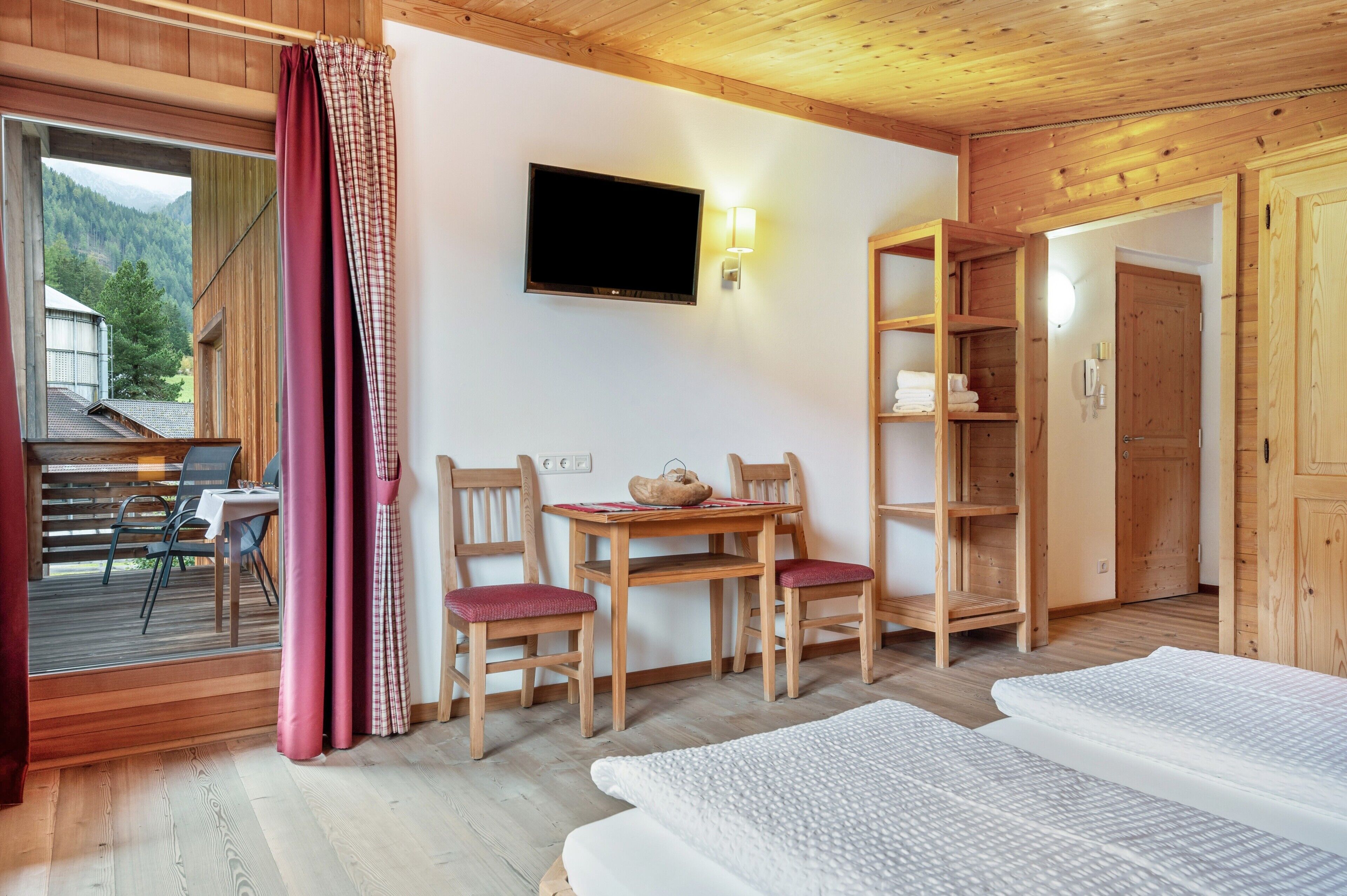 Una habitación de madera con televisión, una mesa con sillas, una estantería y una cama.