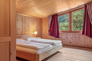A wooden cabin bedroom with a bed, a nightstand, and a window with curtains.