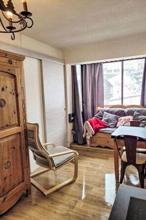 Une pièce chaleureuse avec un meuble en bois, un fauteuil confortable, un lit avec des oreillers et une vue sur un paysage enneigé par la fenêtre.
