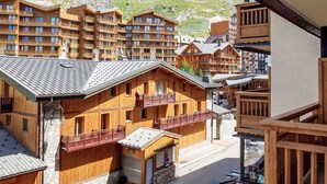 Ein Chalet-ähnliches Gebäude aus Holz mit Balkonen, einer Steinfassade und einem Bergpanorama im Hintergrund.