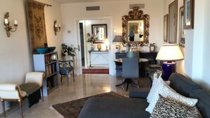 A living room with a sofa, armchairs, a coffee table, a bookshelf, a dining area with a table and chairs, and a kitchen in the background.