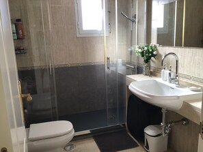 A modern bathroom with a glass-enclosed shower, a white sink, and a toilet.