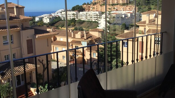 A balcony with a view of a coastal town, featuring terraced buildings and a clear sky.