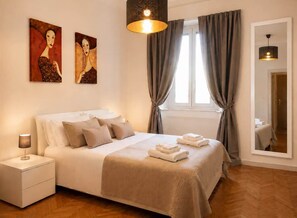 A hotel room with a bed, a nightstand, a lamp, a mirror, and two paintings on the wall. - Civico 37: 3-bedroom apartment in Milan (Milano)