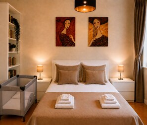 Una habitación de hotel con una cama, dos lámparas de noche, una estantería y dos cuadros en la pared.