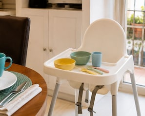 A high chair with a tray table holding a bowl, cup, and utensils.