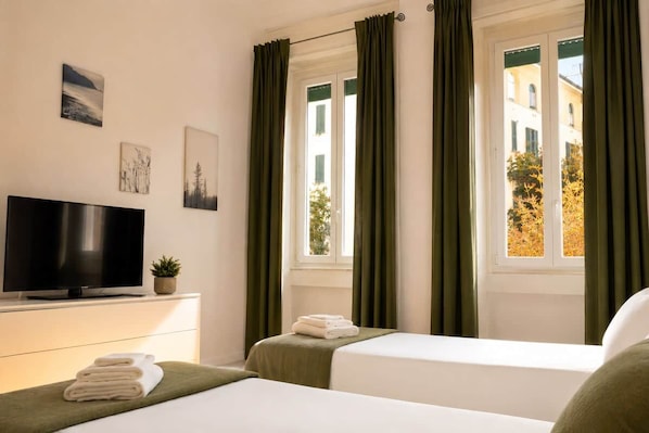 A hotel room with a bed, a TV, and a window with curtains.