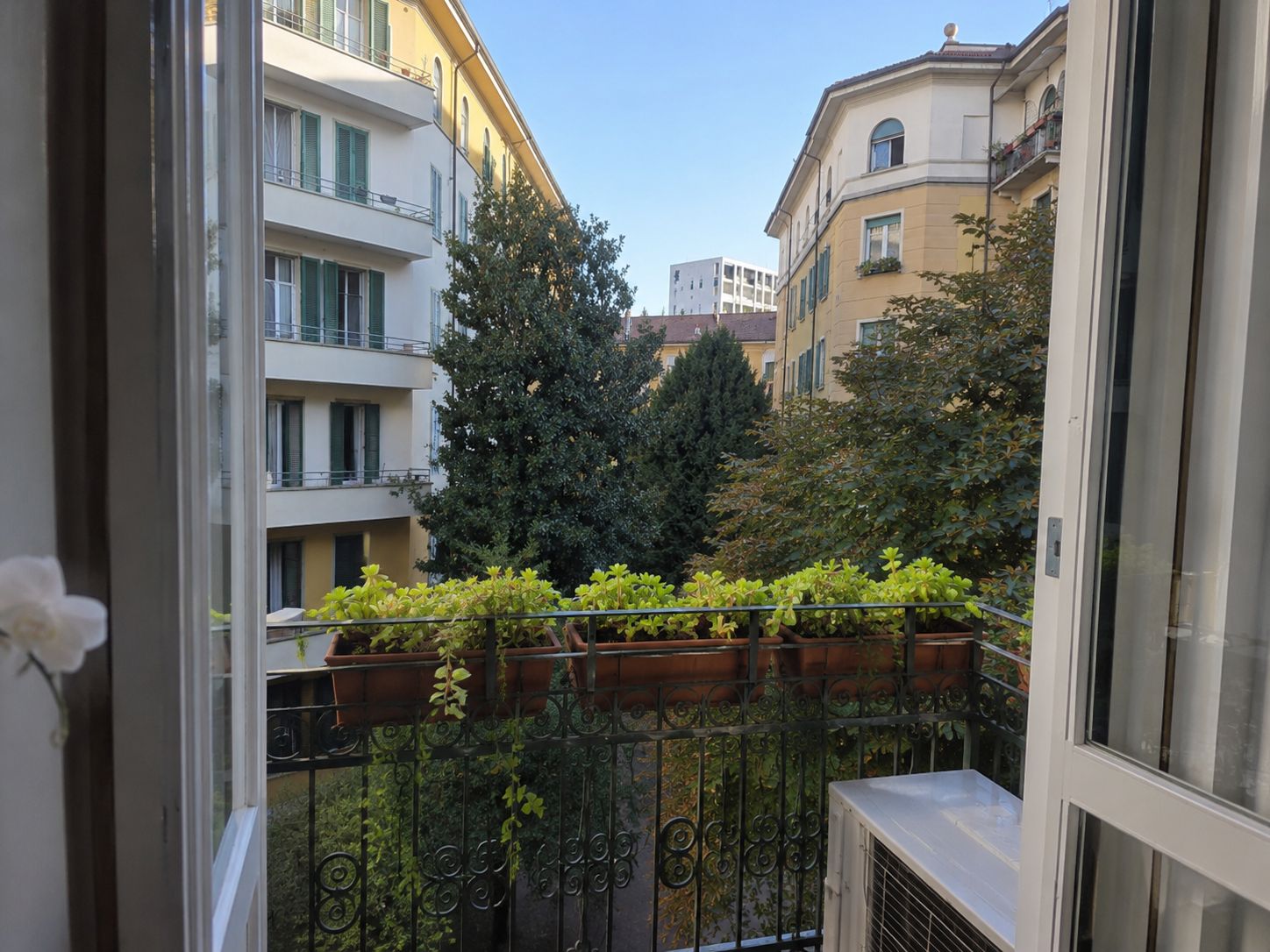Vista da un balcone con ringhiera metallica su una stretta via fiancheggiata da edifici.