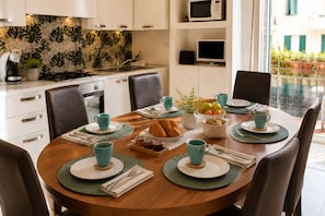Comedor con una mesa redonda dispuesta para cuatro personas, rodeada de sillas, y una cocina al fondo.