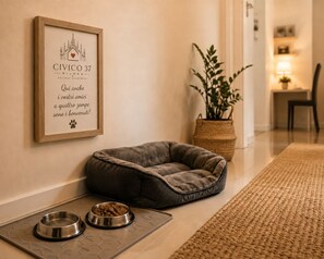 Un espace aménagé pour les animaux de compagnie, avec un panneau encadré, un panier pour animaux et deux gamelles en métal disposées sur un plateau.