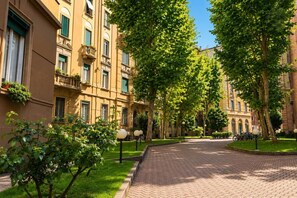 Un chemin pavé bordé d’arbres et d’immeubles dotés de balcons, ce qui laisse supposer qu’il s’agit d’un quartier résidentiel.