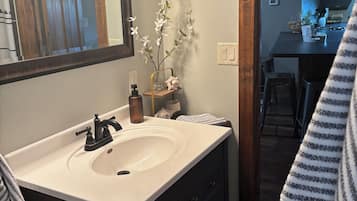 Un baño con lavamanos, espejo y un florero con flores.