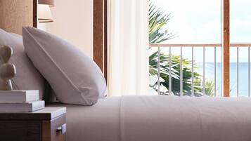 A bedroom with a view of the ocean, a wooden headboard, a bedside table with a lamp, and a pillow.