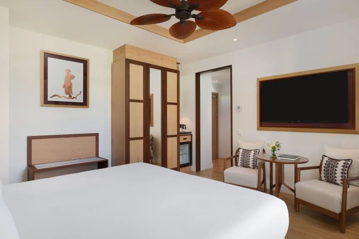 Habitación de hotel con una cama grande, un escritorio, una silla, un televisor y un ventilador de techo.