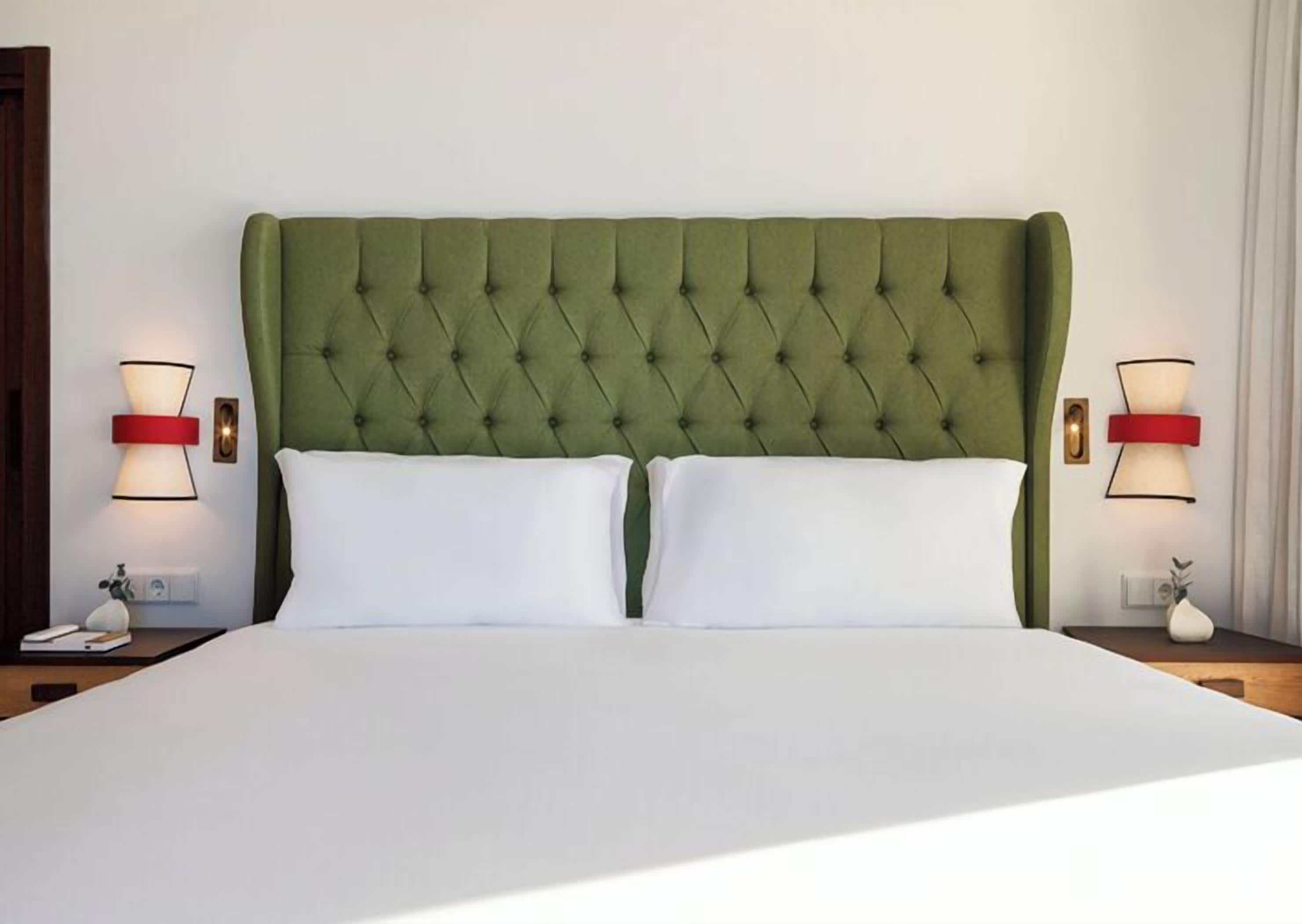 Una cama con cabecera capitonada, dos mesitas de noche y lámparas fijadas a la pared.