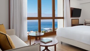 Habitación de hotel con un ventanal grande, una cama, un sofá, una mesita y un ventilador de techo.