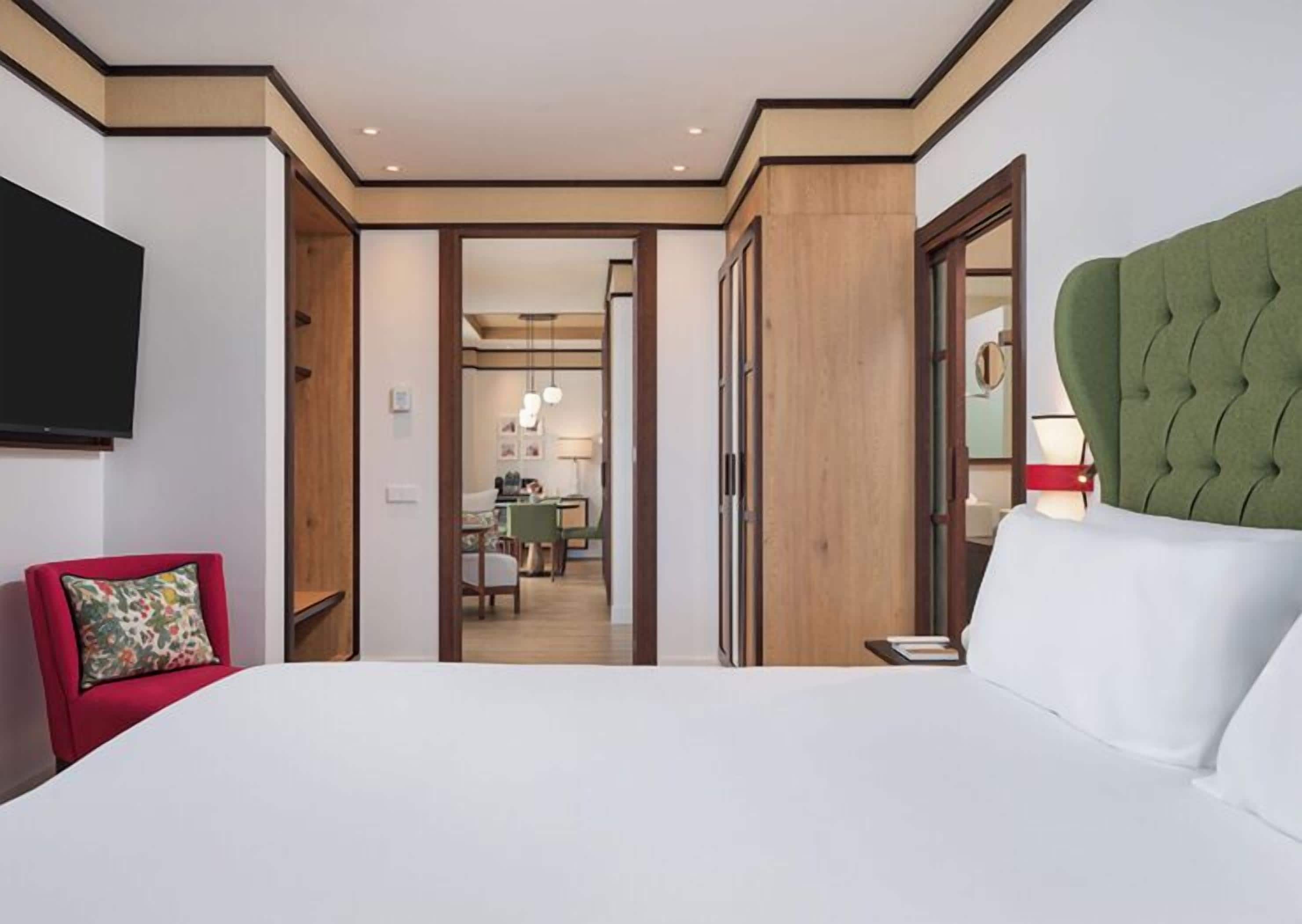 Camera d'albergo con un letto grande, una TV a parete, una sedia rossa e vista sulla sala da pranzo.