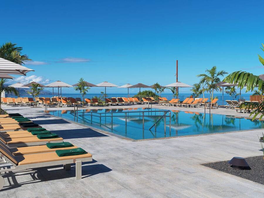 A pool area with lounge chairs and umbrellas, a clear blue sky, and a view of the ocean.
