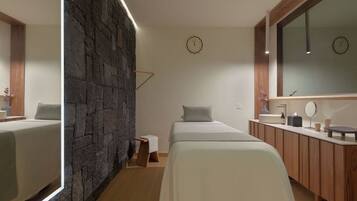 A modern hotel room with a stone accent wall, a large mirror, a bed, a bedside table, and a wooden vanity with a sink.