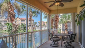A balcony with a table and chairs, overlooking a residential area with palm trees and buildings. - Gorgeous 3B/2B Island Condo At Bella Lago, Pool, Walk To Beach (Fort Myers Beach)