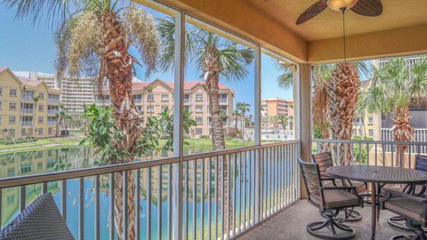 A balcony with a table and chairs, overlooking a pool and palm trees, with buildings in the background. - Gorgeous 3B/2B Island Condo At Bella Lago, Pool, Walk To Beach (Fort Myers Beach)