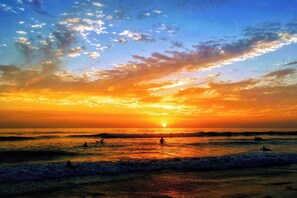 Tramonto su una spiaggia con onde e alcune persone che fanno il bagno.