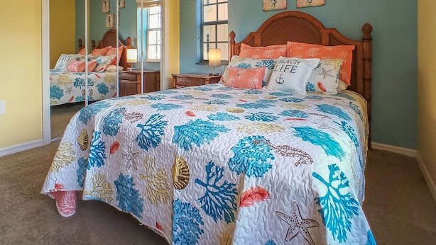 Un dormitorio con cama, mesita de noche, espejo y ventana.
