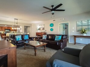 Ein Wohnzimmer mit Couchtisch, zwei Sofas, Deckenventilator und einer Küche im Hintergrund.