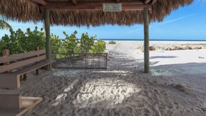 Una cabaña en la playa con techo de paja, un banco de madera y un letrero que indica que es una instalación privada tipo tiki solo para huéspedes.