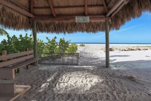Eine Strandhütte mit einem Reetdach, einer Holzbank und einem Schild, das anzeigt, dass es sich um eine private Tiki-Einrichtung nur für Gäste handelt.
