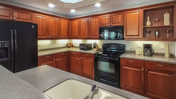 A kitchen with wooden cabinets, a black refrigerator, a microwave, an oven, and a coffee maker. - Gorgeous 3B/2B Island Condo At Bella Lago, Pool, Walk To Beach (Fort Myers Beach)